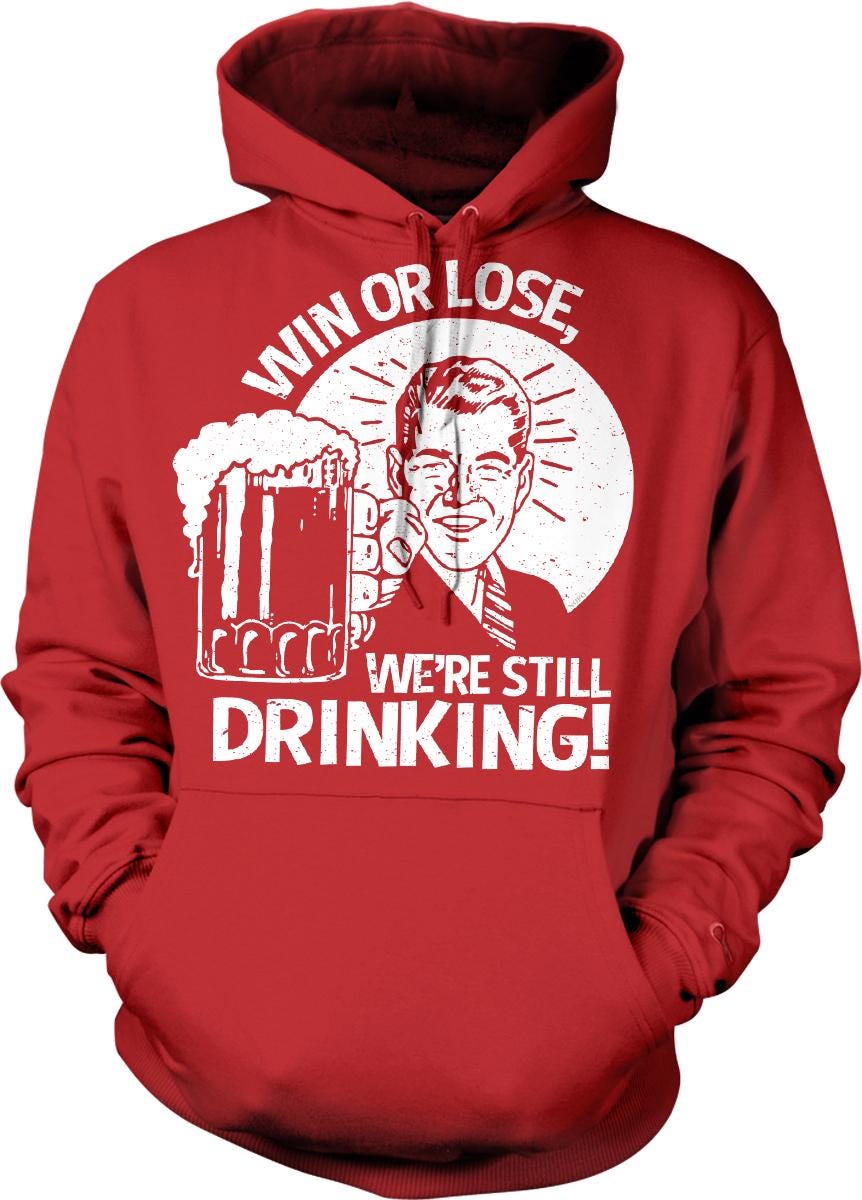 A red hoodie with a graphic design depicting a man holding a beer mug and the text "WIN OR LOSE, WE'RE STILL DRINKING!"