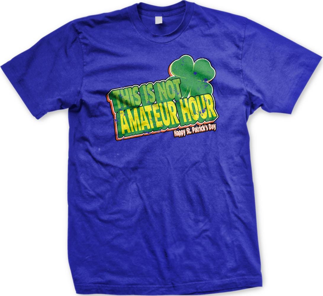 A blue t-shirt with a graphic design featuring a clover and text that reads "This is not amateur hour Happy St. Patrick's Day".