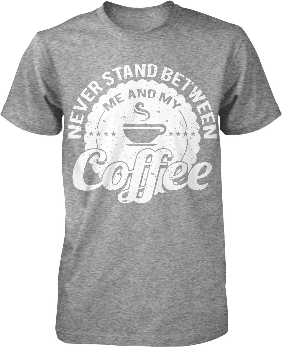 A gray t-shirt with a graphic design that says "NEVER STAND BETWEEN ME AND MY COFFEE" in a circular shape with a coffee cup symbol.