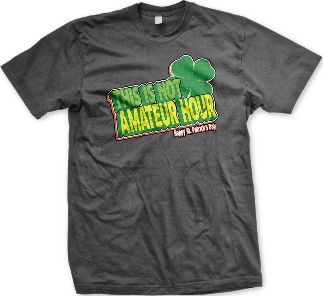 A gray t-shirt with a graphic design featuring a clover and text that reads "This is not Amadeur Hour Happy St. Patrick's Day".