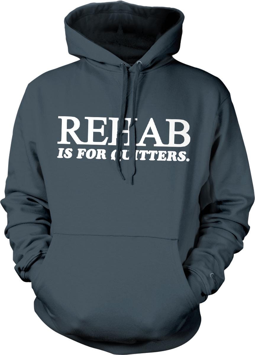A gray hoodie with white text that says "REHAB IS FOR CLUTTER".
